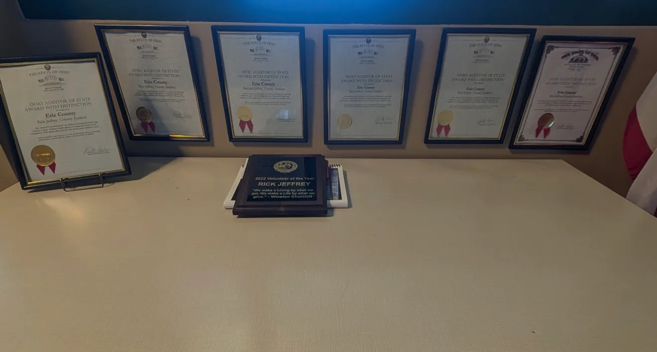 Award certificates and the Rick Jeffrey Volunteer of the Year plaque displayed on a shelf in the auditor's office