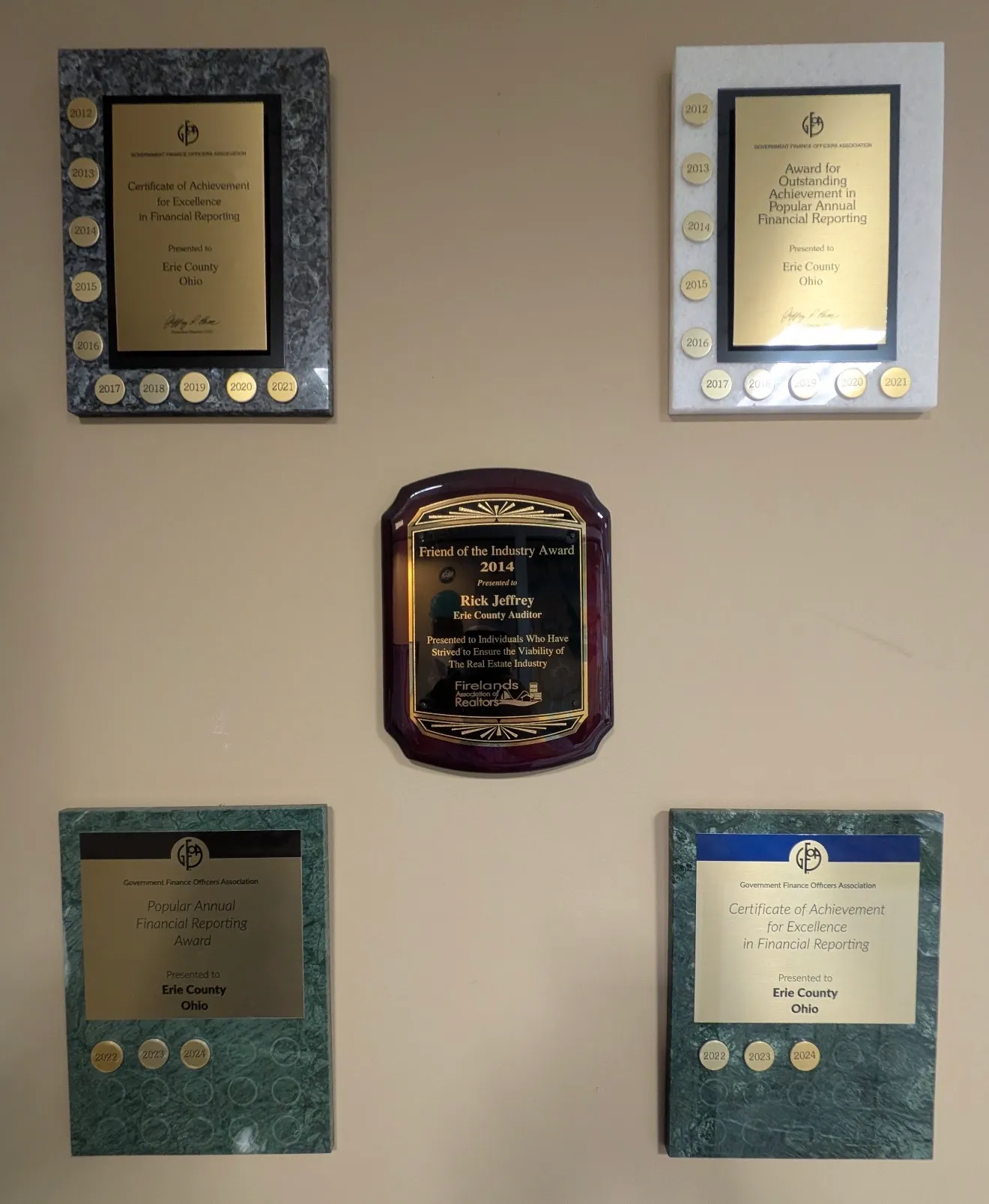 Government Finance Officers Association award plaques for Erie County, Ohio, with year medallions, alongside the 2014 Friend of the Industry Award presented to Rick Jeffrey by the Firelands Association of Realtors